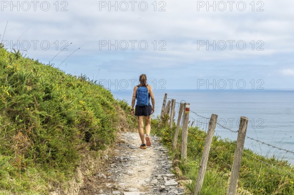 Female tourist walking along a coastal path in zumaia, basque country, enjoying the scenic view of the ocean