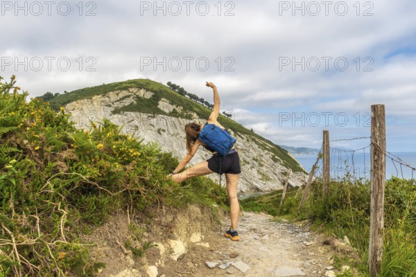 Female hiker stretching leg on a trail overlooking sakoneta beach and flysch cliffs in zumaia, gipuzkoa, basque country, spain