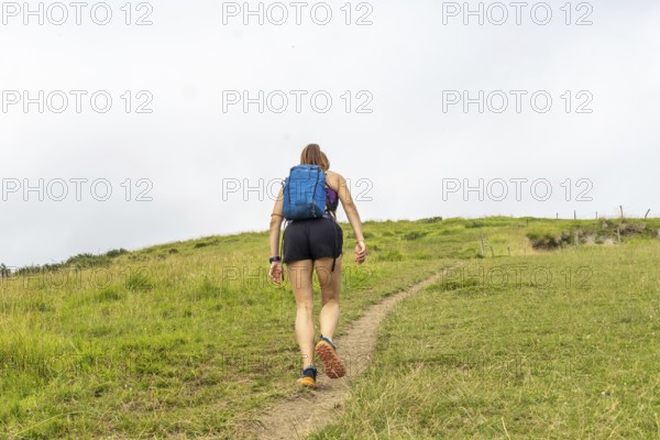 Female tourist walking up the grassy hill at sakoneta beach near zumaia in the basque country, spain, exploring the unique flysch rock formations