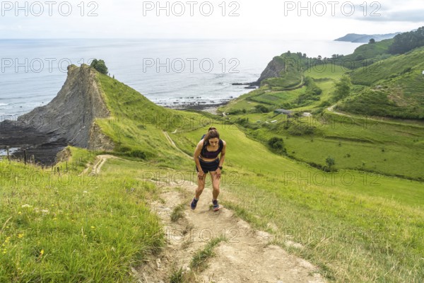 Tired athlete taking a break during trail running workout along the picturesque cliffs of zumaia, basque country, spain, enjoying scenic coastal views