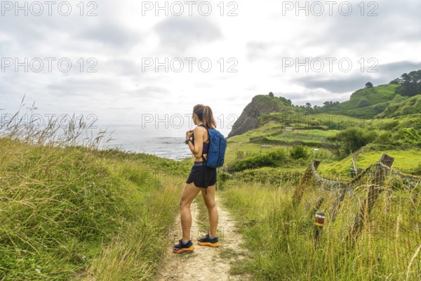 Female hiker enjoying the scenic view of sakoneta beach and its flysch cliffs in zumaia, gipuzkoa, during a summer hike in the basque country