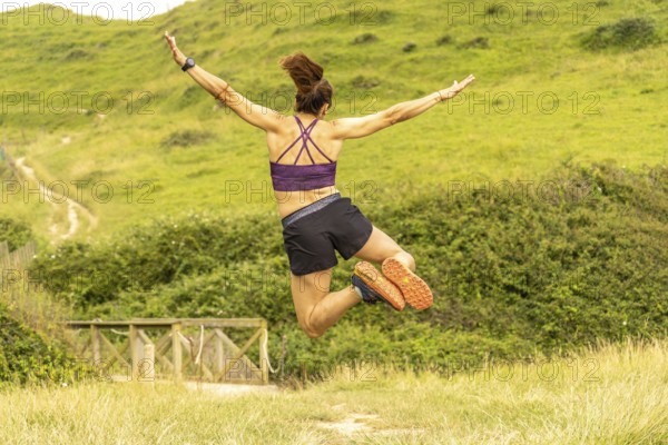 Runner celebrates reaching the top of a hill overlooking sakoneta beach and the flysch cliffs in zumaia, basque country