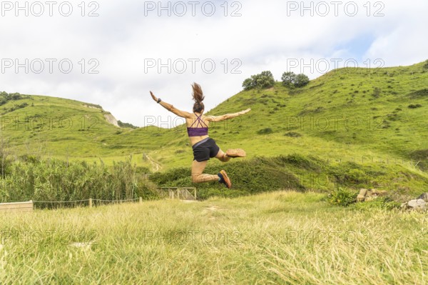 Sporty woman jumping with outstretched arms in a beautiful natural landscape in zumaia, gipuzkoa, celebrating achievement and freedom