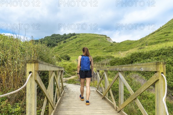 Female tourist with backpack walking on a wooden bridge near sakoneta beach and its flysch in zumaia, basque country