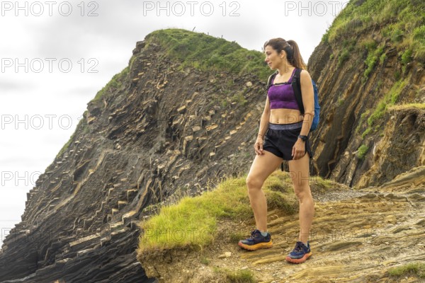 Female hiker admiring the breathtaking flysch cliffs at sakoneta beach in zumaia, gipuzkoa, a unique geological formation on the basque coast