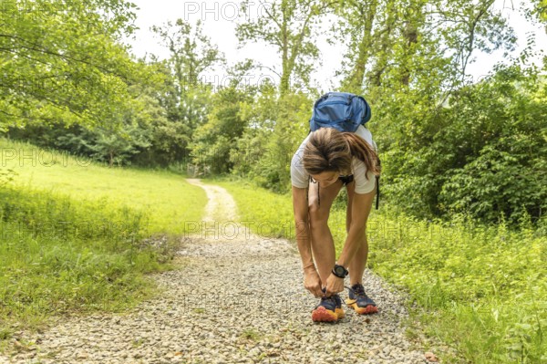 Female hiker tying her shoelaces before starting her trekking activity on a gravel path in a forest