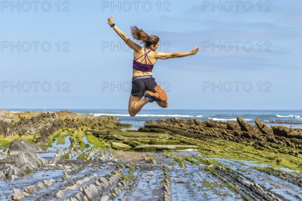 Celebrating freedom and athleticism, a woman leaps with joy amidst the unique geological formations of sakoneta beach's flysch cliffs in zumaia, basque country