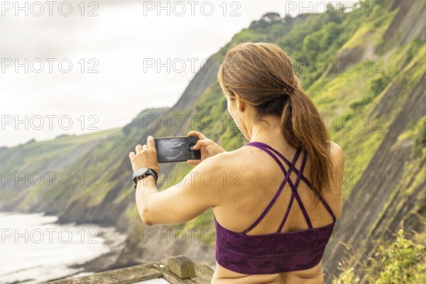 Sportswoman taking photos of the itzurun beach from the sakoneta viewpoint in zumaia, basque country
