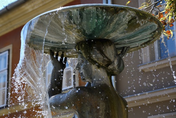 Water flowing from a basin held by a beautifully crafted statue, creating dynamic jets and splashes in an elegant urban fountain