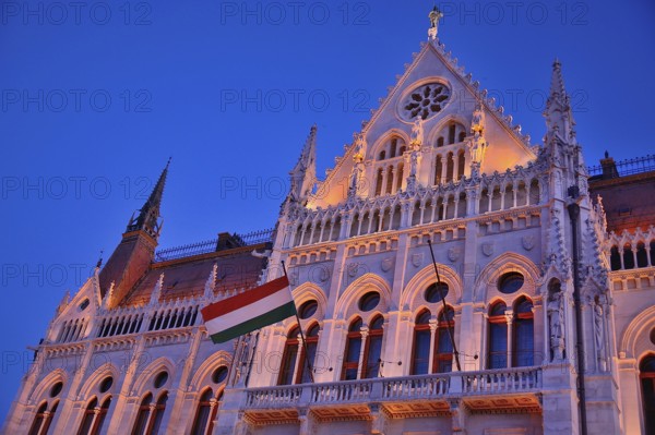 Ornate facade of hungarian parliament building illuminated at twilight with hungarian flag waving, budapest, hungary