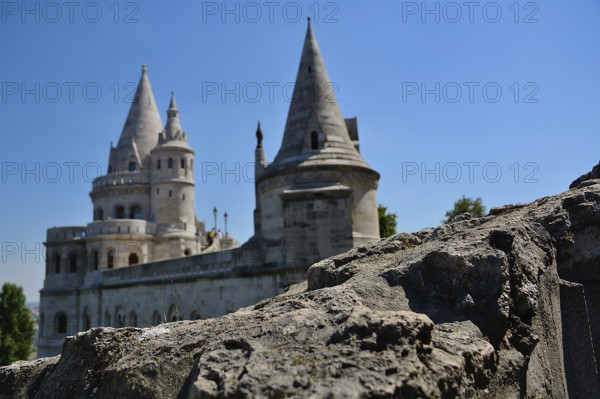 Stone wall in the foreground with the fisherman's bastion standing tall against a clear blue sky, showcasing the architectural beauty of budapest