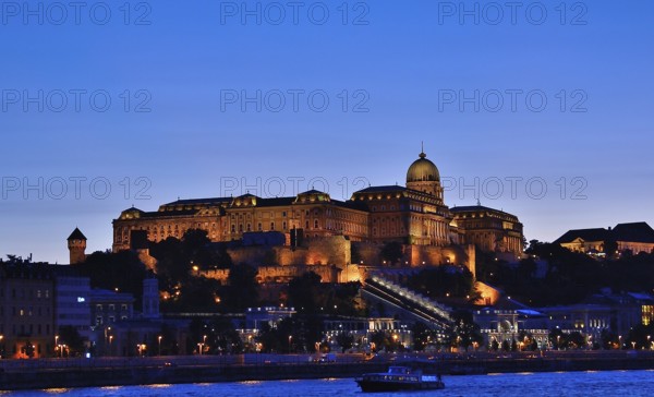 Buda castle, a historic landmark in budapest, hungary, is illuminated against the twilight sky, with the danube river reflecting the city lights