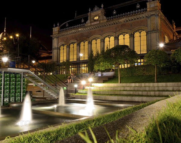 Nyugati palyaudvar, a beautifully illuminated train station in budapest, stands majestically at night, complemented by the soothing presence of fountains in the foreground