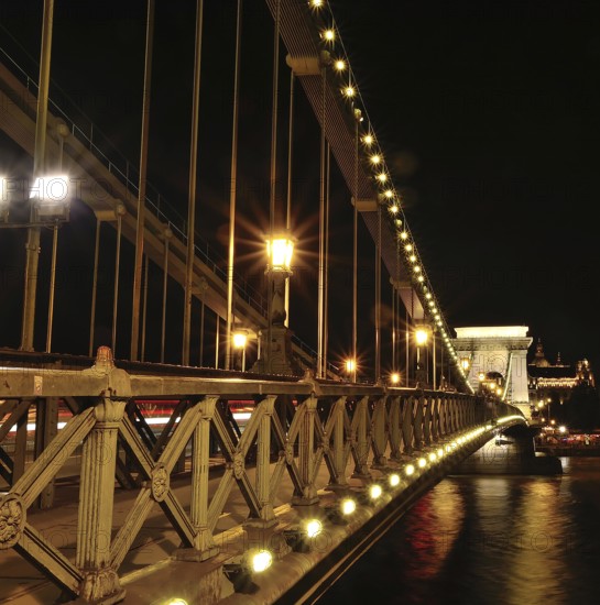 Chain bridge glowing beautifully at night, showcasing blurred car light trails against the backdrop of budapest's enchanting cityscape