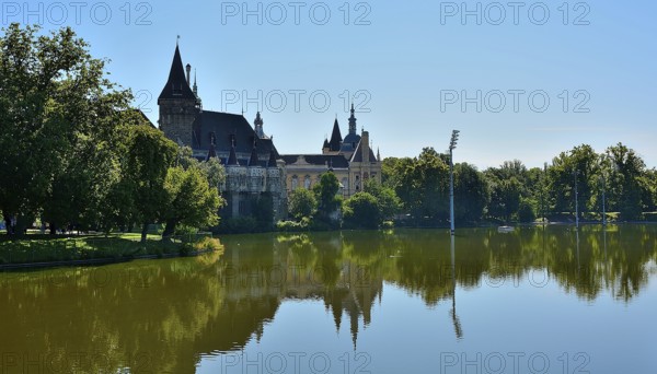 Vajdahunyad castle reflecting beautifully on the lake in budapest's city park, surrounded by lush trees on a sunny summer day