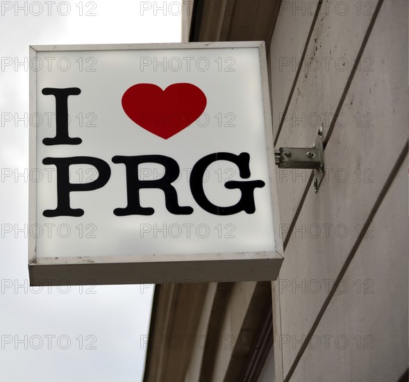White square sign with i love prg written on it, hanging on a building facade, expressing affection for prague