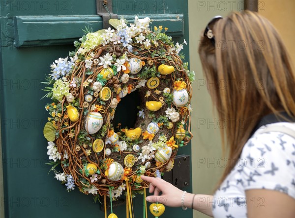 Tourist touching a colorful easter wreath with ceramic eggs and chicks hanging on a green door in prague or budapest