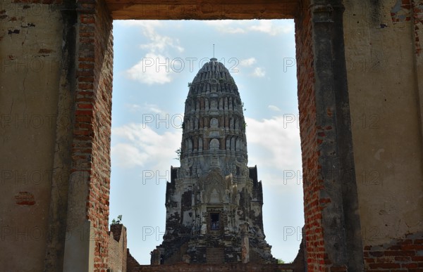 Crumbling brick walls frame a majestic ancient prang under a partly cloudy sky, showcasing the rich history and architectural heritage of thailand