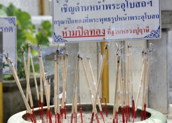 Incense sticks are burning, creating a fragrant smoke, in a pot at a temple in thailand, symbolizing prayer and reverence