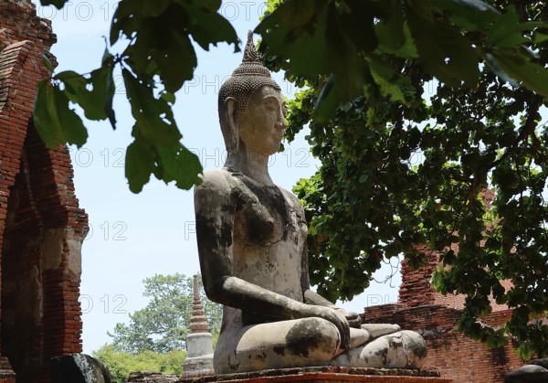 Serene buddha statue sits in peaceful meditation amidst crumbling temple ruins, showcasing thailand's rich spiritual and architectural heritage