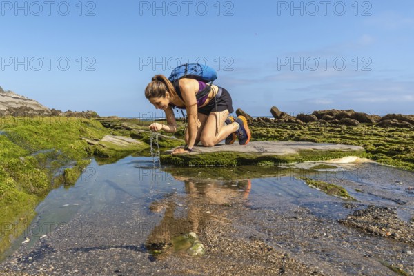 Female hiker refreshing with water from a puddle on the flysch rock formations of sakoneta beach in zumaia, basque country, spain