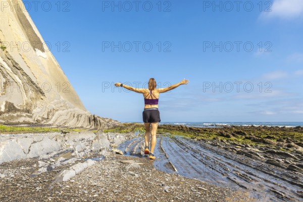 Female athlete enjoying freedom and nature, walking on the unique rock formations of sakoneta beach at low tide, with open arms towards the sea