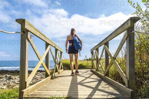 Hiker walking on a wooden walkway leading to sakoneta beach in zumaia, basque country, with flysch cliffs and blue sea in background