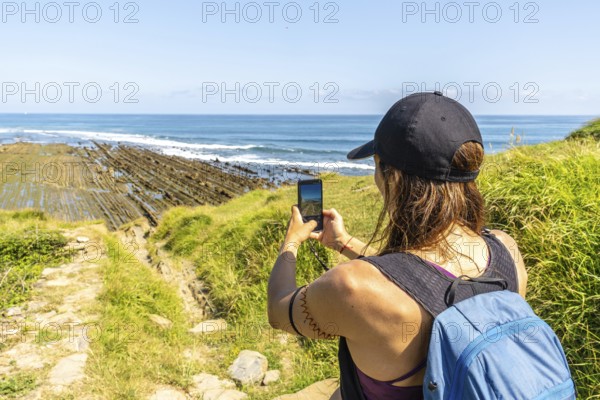 Hiker taking pictures of the impressive flysch cliffs at sakoneta beach in zumaia, basque country, spain, a unique geological formation