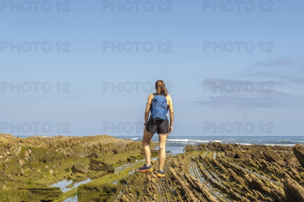 Female hiker with backpack admiring the stunning coastal rock formations of the zumaia flysch on sakoneta beach, gipuzkoa, basque country