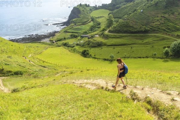 Female hiker walking down a path in the hills near sakoneta beach in zumaia, basque country, spain, enjoying the scenic view of the flysch cliffs and the ocean