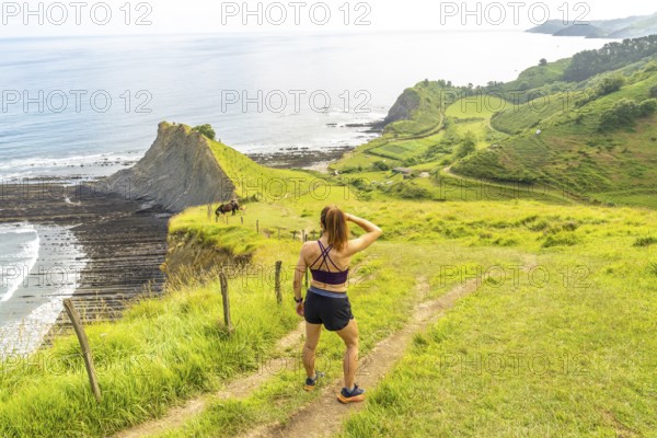 Female athlete enjoying the view of the sakoneta beach and its coastal flysch in zumaia, gipuzkoa