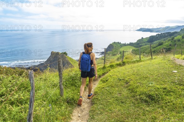 Female hiker enjoying the stunning view of sakoneta beach and its coastal flysch in zumaia, basque country, spain, during a sunny summer day