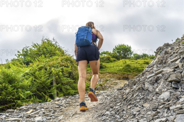 Female hiker ascending a steep, rocky trail in zumaia, basque country, showcasing the rugged beauty of the flysch cliffs