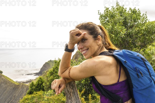 Female hiker with backpack taking a break and enjoying the breathtaking view of sakoneta beach and flysch cliffs in zumaia, basque country