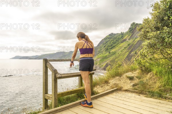 Female tourist consulting informative map at viewpoint in sakoneta beach, next to flysch in zumaia, basque country, spain