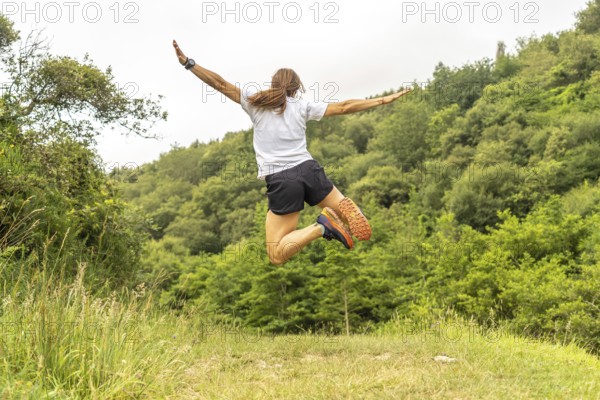 Celebrating athletic achievement, a female athlete jumps with outstretched arms in a vibrant green meadow near zumaia, basque country, expressing pure joy and freedom