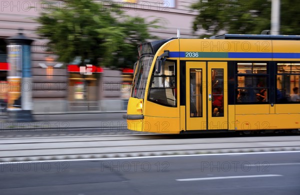 Yellow tram speeding through the bustling city center, showcasing motion blur and filled with passengers enjoying their commute