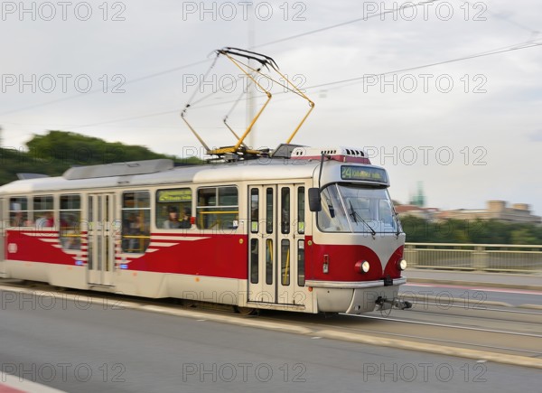 Red and white tram carrying passengers is crossing a bridge in prague, czech republic, providing urban transportation