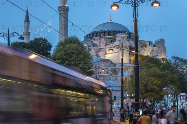 Tram gliding past the iconic hagia sophia in sultanahmet square during the enchanting blue hour in istanbul, turkey