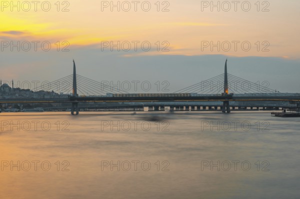 Long exposure of a metro train crossing the golden horn metro bridge in istanbul, turkey, during a beautiful sunset