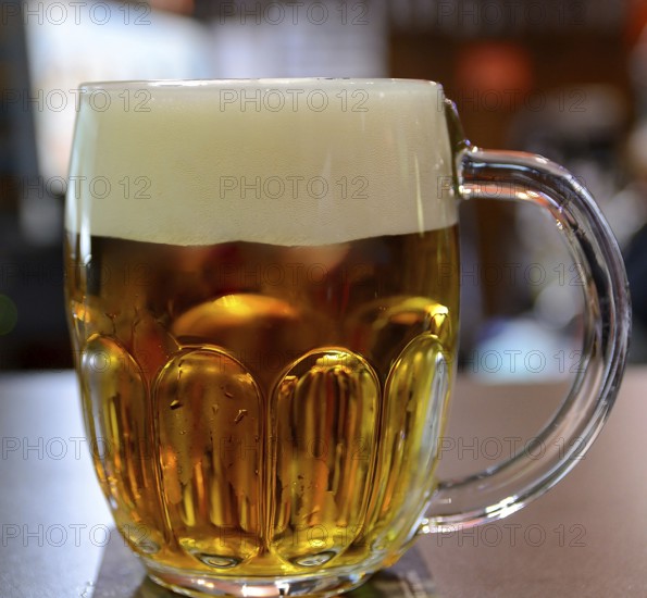 Large glass mug full of cold, golden beer with a thick head, creating a refreshing scene in a pub, possibly located in prague or budapest