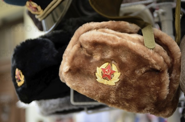 Traditional russian winter hats, known as ushankas, adorned with soviet badges, are displayed for sale in a souvenir shop, likely in prague or budapest