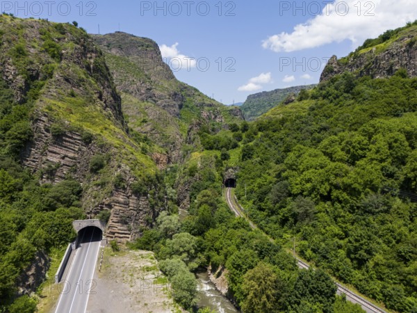 Road tunnel and railway tunnel through forested mountain landscape under blue sky, aerial view, landscape near Dzoraget, Pambak river, Debed gorge, Lorikeet province, Armenia