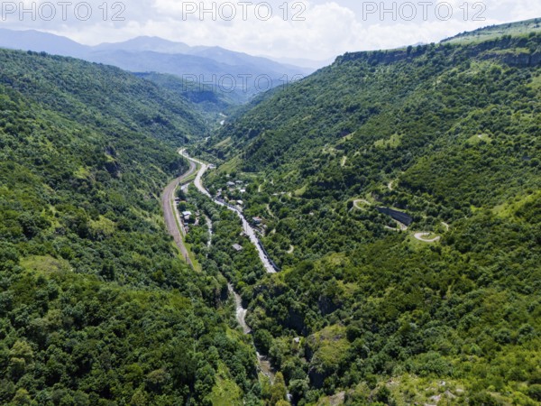 A green valley with dense vegetation, a road and a river between mountain ranges under a cloudy sky, aerial view, landscape near Dzoraget, Pambak River, Lorikeet Province, Armenia