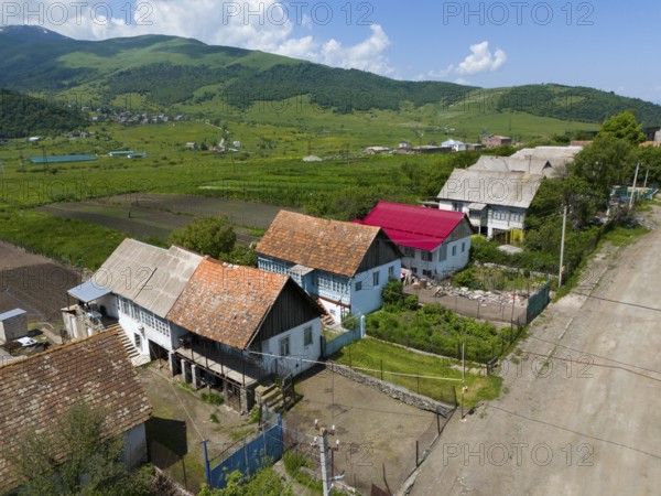 Colourful row of houses on a country road with fields and green hills in the background, aerial view, Lermontovo, inhabited by spiritual Christians Pryguny and Molokans from Russia, Lorikeet Province, Armenia