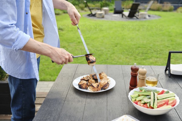 Unrecognizable man removes grilled meat from skewer to a plate. The concept of a picnic in the backyard