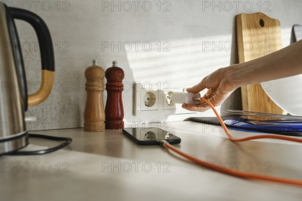 A person plugs a smartphone charger into an outlet while standing in a stylish kitchen