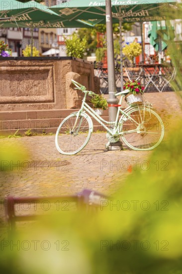 A white bicycle stands decoratively in front of a fountain in the town, small town of Perle Calw, Black Forest, Germany