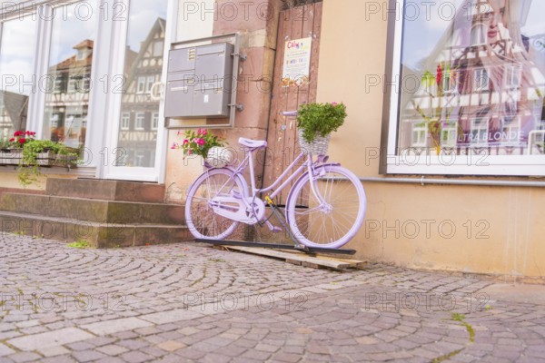 A purple bicycle with a basket of flowers in front of a building with half-timbered houses, small town of Perle Calw, Black Forest, Germany