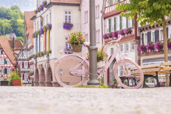 Pink bicycle with flower pots in front of historic half-timbered houses on a cobbled town square, small town of Perle Calw, Black Forest, Germany